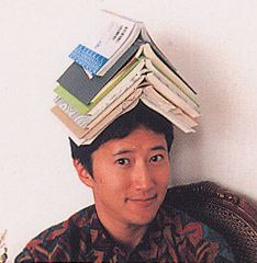 araki hirohiko, lowres, photo (medium), tagme, 1boy, black hair, book, book stack, collared shirt, looking at viewer, mangaka, portrait, shirt, short hair, smile, wing collar