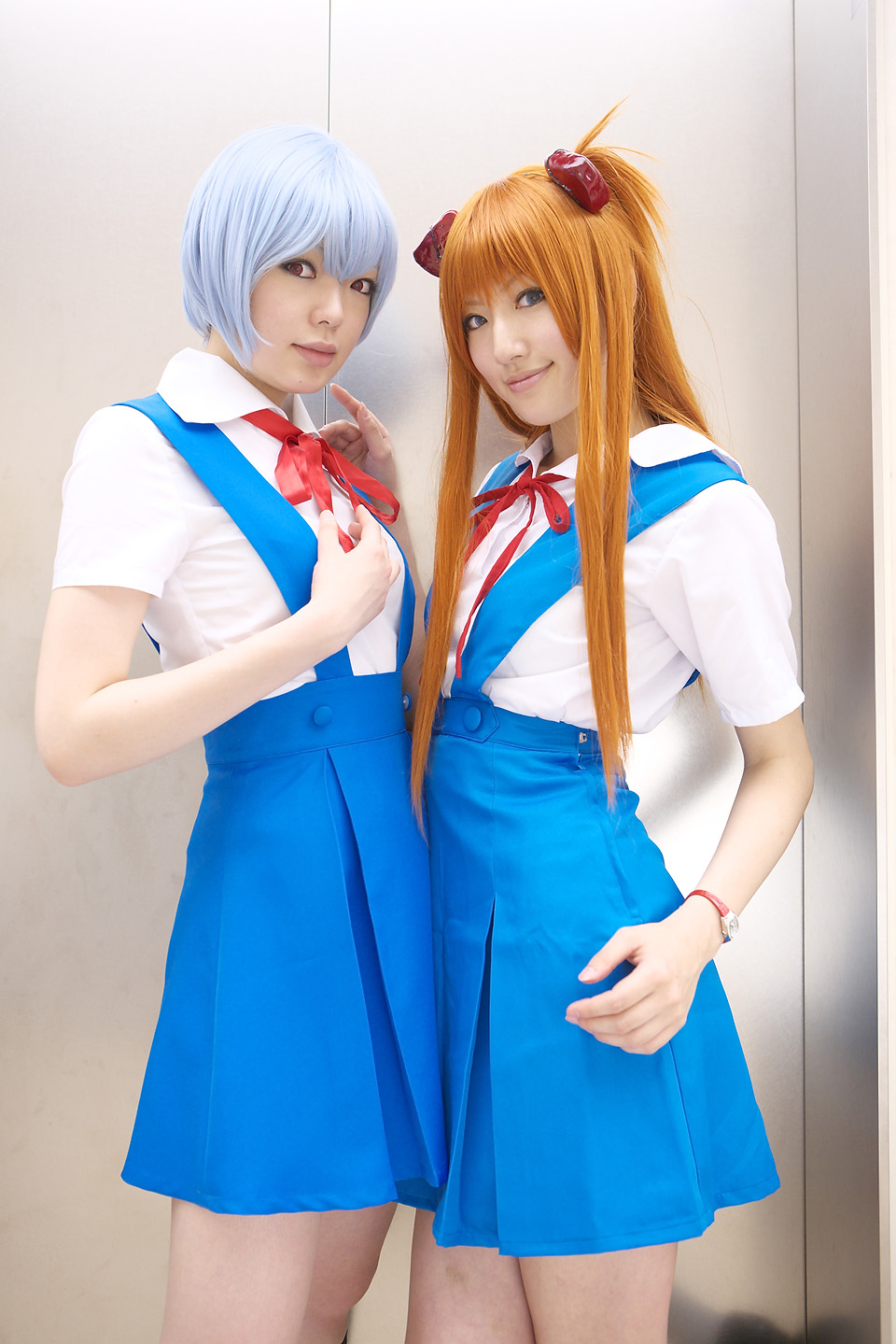 namada, saya (cosplayer), ayanami rei, souryuu asuka langley, neon genesis evangelion, highres, photo (medium), 2girls, asian, ayanami rei (cosplay), blue eyes, blue hair, breasts, color contacts, cosplay, cowboy shot, indoors, long hair, looking at viewer, makeup, mascara, miniskirt, multiple girls, orange hair, red eyes, school uniform, short hair, skirt, small breasts, smile, souryuu asuka langley (cosplay), standing