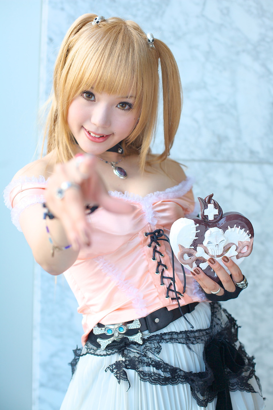 kipi-san, amane misa, death note, highres, photo (medium), 1girl, amane misa (cosplay), asian, bare shoulders, blonde hair, breasts, choker, color contacts, cosplay, cross, female focus, fingerless gloves, gloves, hair ornament, indoors, jewelry, long hair, looking at viewer, miniskirt, mole, pendant, pointing, pointing at viewer, ring, single glove, skirt, skull and crossbones, skull hair ornament, skull ring, small breasts, smile, solo, two side up