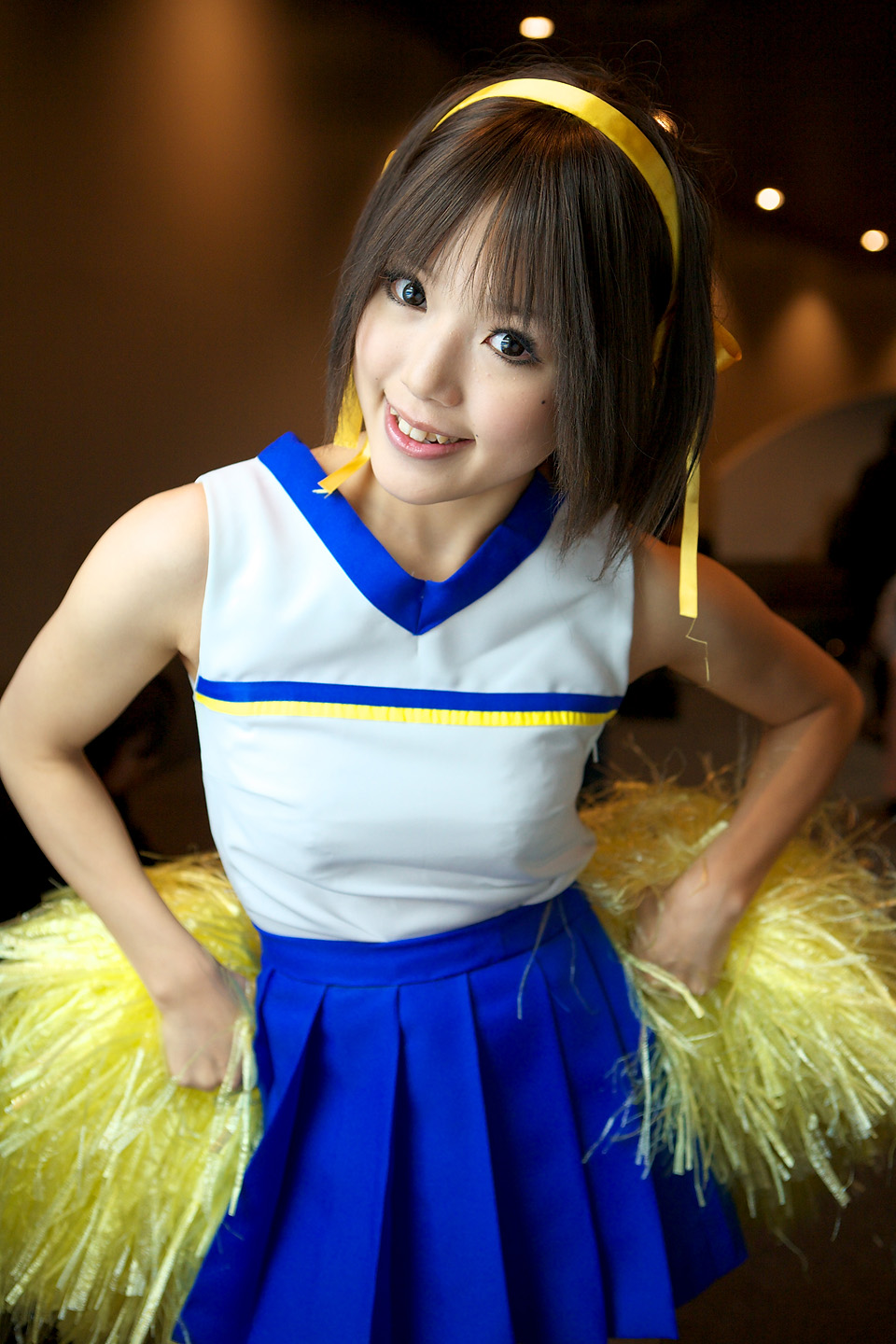 kipi-san, suzumiya haruhi, suzumiya haruhi no yuuutsu, highres, photo (medium), 1girl, asian, brown eyes, brown hair, cheerleader, cosplay, female focus, indoors, looking at viewer, mole, pom pom (cheerleading), smile, solo, suzumiya haruhi (cosplay)