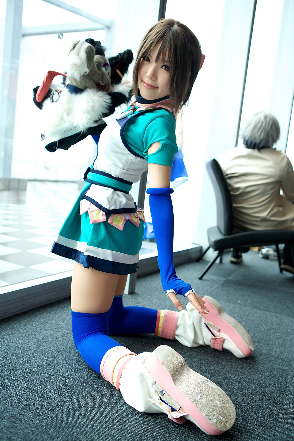 kipi-san, branky, mel, gensou suikoden, highres, photo (medium), 1girl, asian, blue gloves, blue thighhighs, brown eyes, brown hair, cosplay, elbow gloves, fingerless gloves, gloves, kneeling, looking at viewer, looking back, mel (cosplay), mole, puppet, short hair, smile, solo focus, stuffed animal, stuffed toy, thighhighs, zettai ryouiki