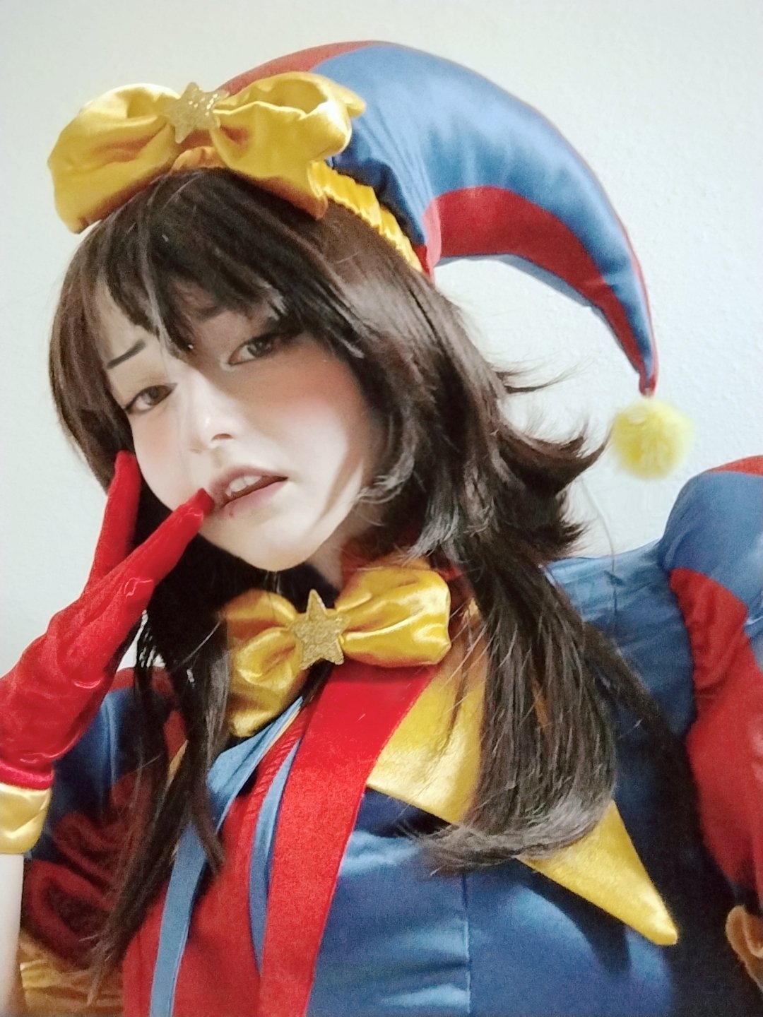 unkyndled, pomni (the amazing digital circus), glitch productions, real life, the amazing digital circus, photo (medium), 1girl, cosplay, hat, indoors, jester cap, lips, looking at viewer, open mouth, parted lips, pomni (the amazing digital circus) (cosplay), selfie, short hair, upper body