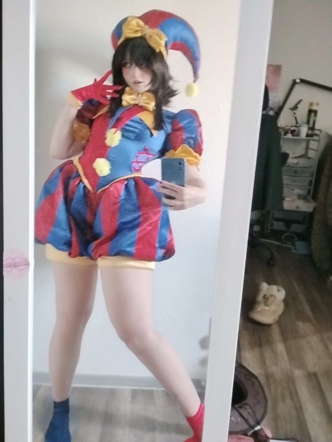 unkyndled, pomni (the amazing digital circus), glitch productions, real life, the amazing digital circus, photo (medium), 1girl, cosplay, hat, holding, holding phone, indoors, jester cap, lips, open mouth, phone, pomni (the amazing digital circus) (cosplay), selfie, short hair, wide hips