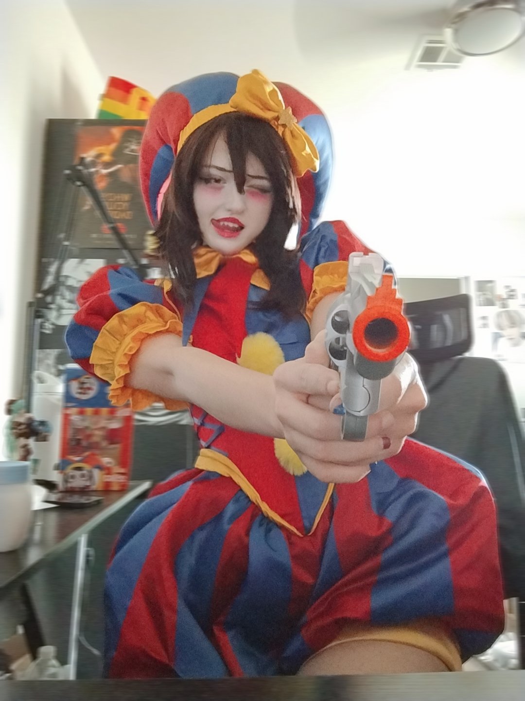 unkyndled, pomni (the amazing digital circus), glitch productions, real life, the amazing digital circus, photo (medium), 1girl, aiming, aiming at viewer, cosplay, gun, hat, indoors, jester cap, licking lips, looking at viewer, open mouth, pomni (the amazing digital circus) (cosplay), short hair, tongue, tongue out, toy gun, weapon, wide hips