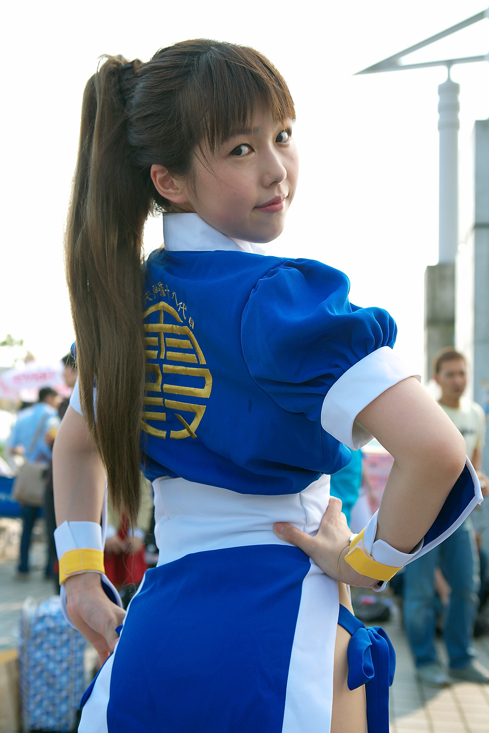 kasumi (doa), koa, dead or alive, tecmo, highres, photo (medium), tagme, 1girl, asian, blurry, brown hair, clothes writing, cosplay, depth of field, from behind, hands on own hips, kasumi (doa) (cosplay), long hair, looking at viewer, looking back, multiple boys, outdoors, panties, pelvic curtain, ponytail, side-tie panties, solo focus, underwear