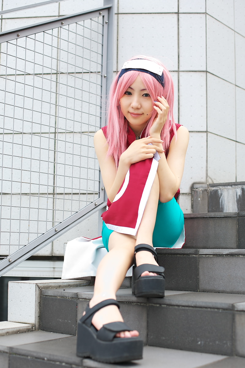 haruno sakura, naruto (classic), naruto (series), highres, photo (medium), 1girl, asian, bare shoulders, bike shorts, black eyes, black shoes, cosplay, dress, earrings, female focus, full body, haruno sakura (cosplay), jewelry, looking at viewer, mole, outdoors, pink hair, red dress, shoes, short hair, shorts, side slit, sitting, skin tight, sleeveless, sleeveless dress, smile, solo, spandex, stairs