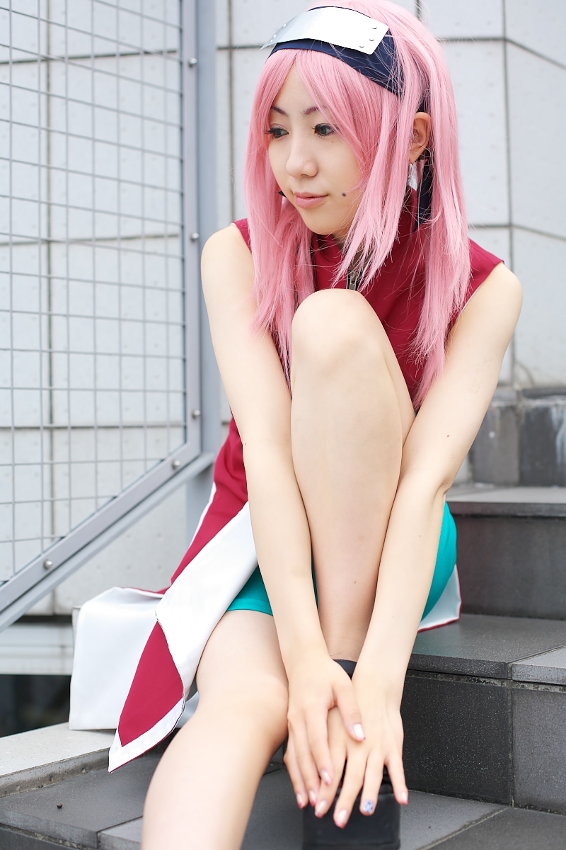 haruno sakura, naruto (classic), naruto (series), highres, photo (medium), 1girl, asian, bare arms, bare shoulders, bike shorts, black eyes, black shoes, cosplay, dress, earrings, eyelashes, female focus, haruno sakura (cosplay), headband, headdress, jewelry, light smile, looking to the side, mole, pink hair, red dress, shoes, short hair, shorts, sleeveless, sleeveless dress, smile, solo, stairs