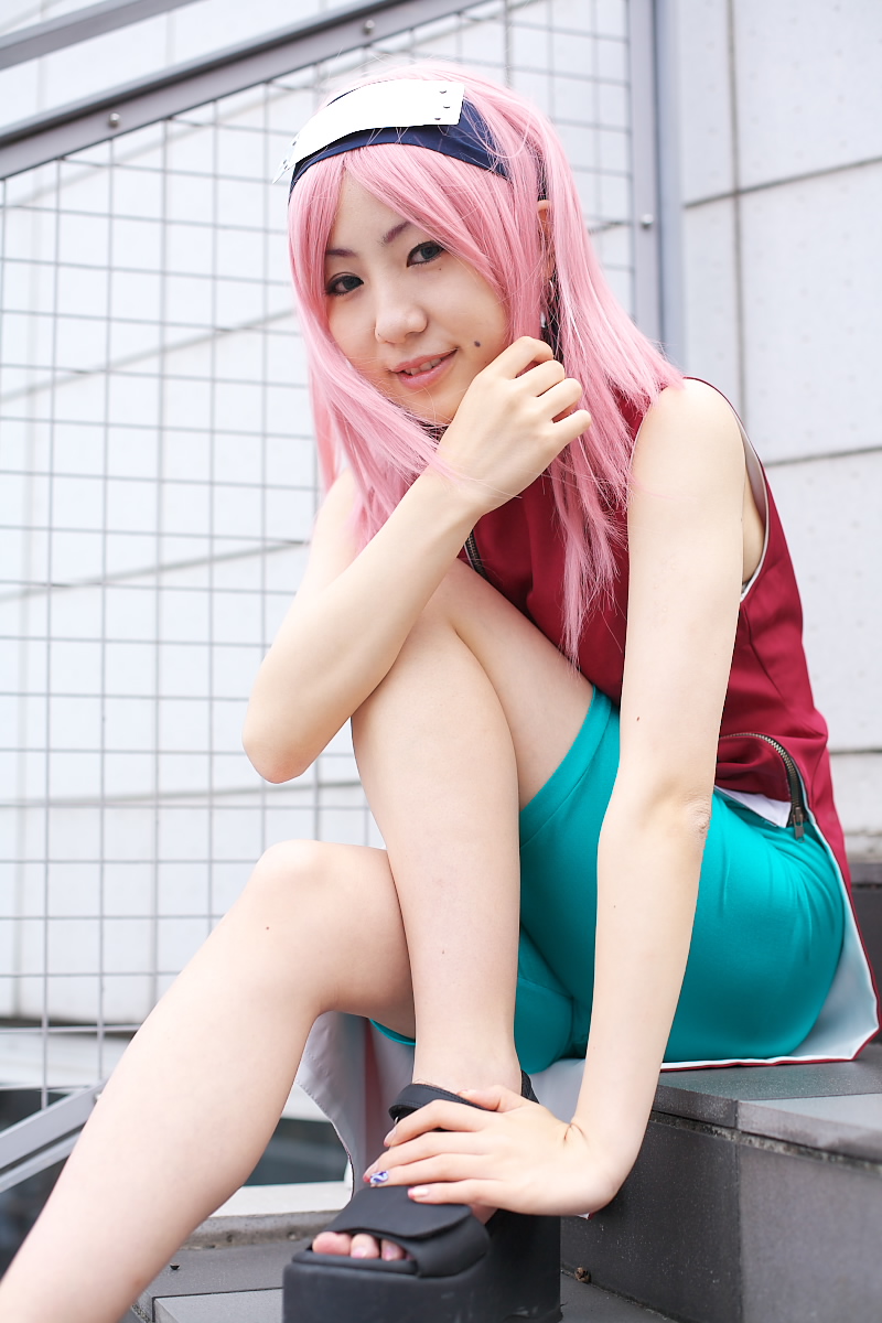 haruno sakura, naruto (classic), naruto (series), highres, photo (medium), 1girl, asian, bare shoulders, bike shorts, black eyes, cosplay, dress, earrings, female focus, fingernails, haruno sakura (cosplay), headband, headdress, jewelry, legs, looking at viewer, mole, nail polish, outdoors, pink hair, red dress, short hair, shorts, side slit, sitting, skin tight, sleeveless, sleeveless dress, smile, solo, spandex, stairs