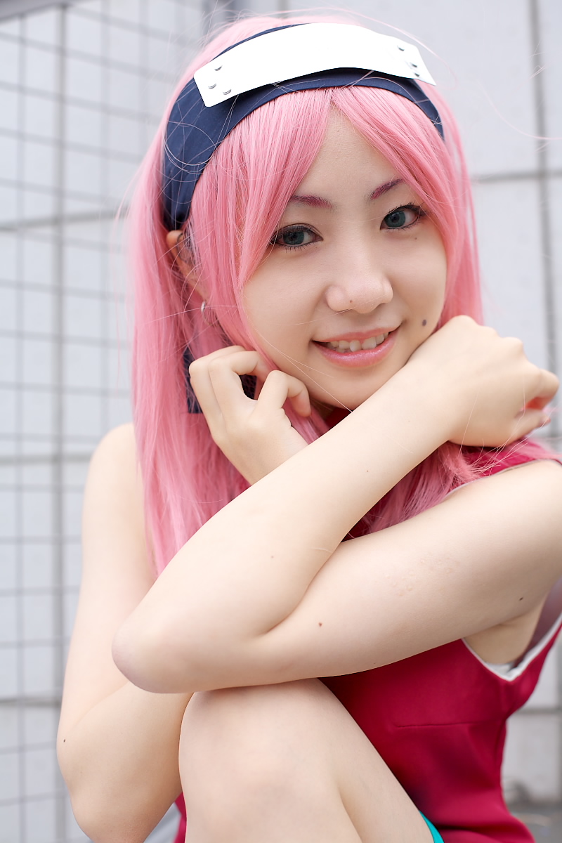 haruno sakura, naruto (classic), naruto (series), highres, photo (medium), 1girl, asian, bare shoulders, black eyes, cosplay, dress, earrings, eyelashes, female focus, haruno sakura (cosplay), headband, headdress, jewelry, knee up, lips, looking at viewer, mole, outdoors, parted lips, pink hair, red dress, short hair, sitting, sleeveless, sleeveless dress, smile, solo, teeth