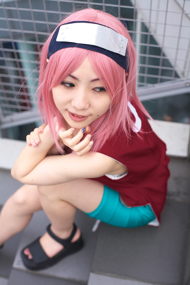 haruno sakura, naruto (classic), naruto (series), highres, photo (medium), 1girl, asian, bare shoulders, bike shorts, black eyes, black shoes, blurry, cosplay, depth of field, dress, eyelashes, female focus, fingernails, haruno sakura (cosplay), headband, headdress, lips, long hair, looking to the side, mole, nail polish, outdoors, parted lips, pink hair, red dress, shoes, shorts, side slit, sitting, sleeveless, sleeveless dress, solo, spandex, stairs