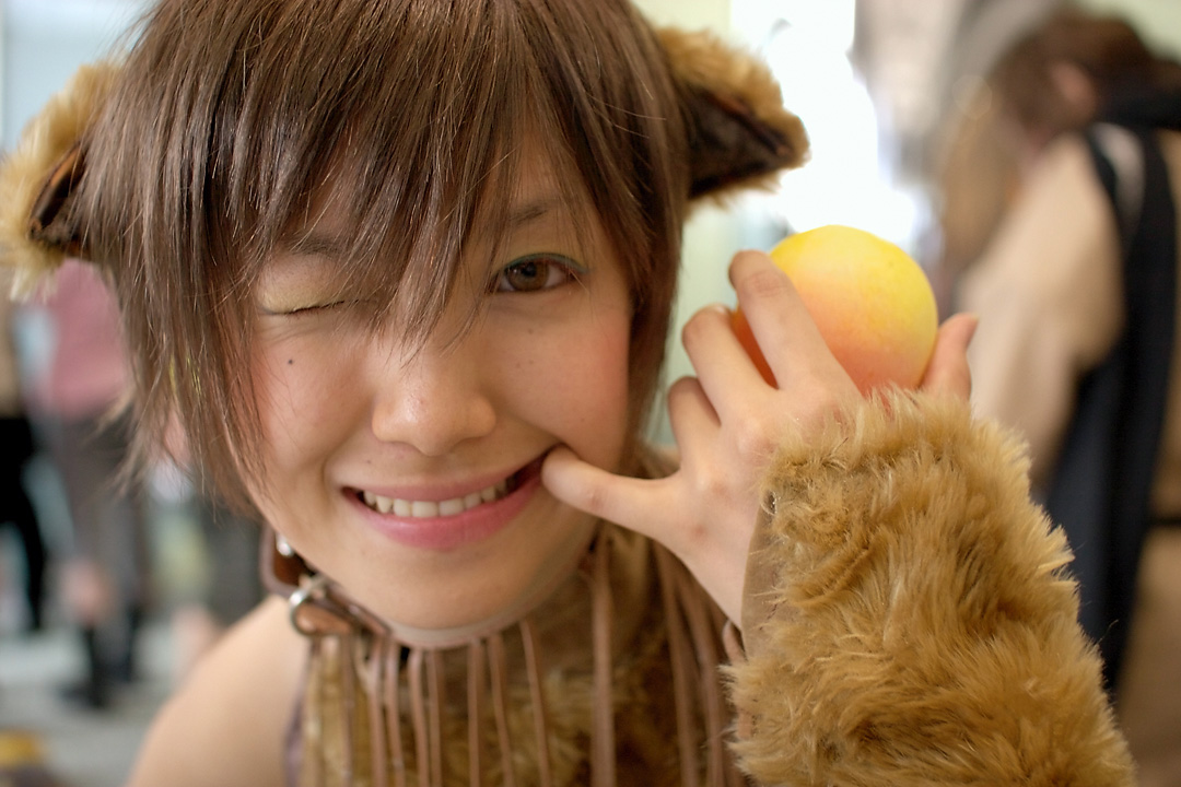namako, tm revolution, wild rush, fur, photo (medium), 1girl, animal collar, animal ears, asian, bare shoulders, blurry, brown eyes, brown hair, choker, collar, cosplay, depth of field, dog ears, fake animal ears, female focus, food, fringe trim, fruit, indoors, looking at viewer, matching hair/eyes, mole, mouth pull, one eye closed, peach, short hair, solo, wink