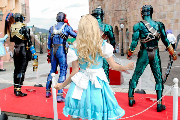 kipi-san, alice (alice in wonderland), kamen rider hibiki, alice's adventures in wonderland, kamen rider, kamen rider hibiki (series), photo (medium), 1girl, 4boys, alice (alice in wonderland) (cosplay), apron, asian, blonde hair, cosplay, crossover, from behind, hair ribbon, long hair, multiple boys, outdoors, petite, ribbon