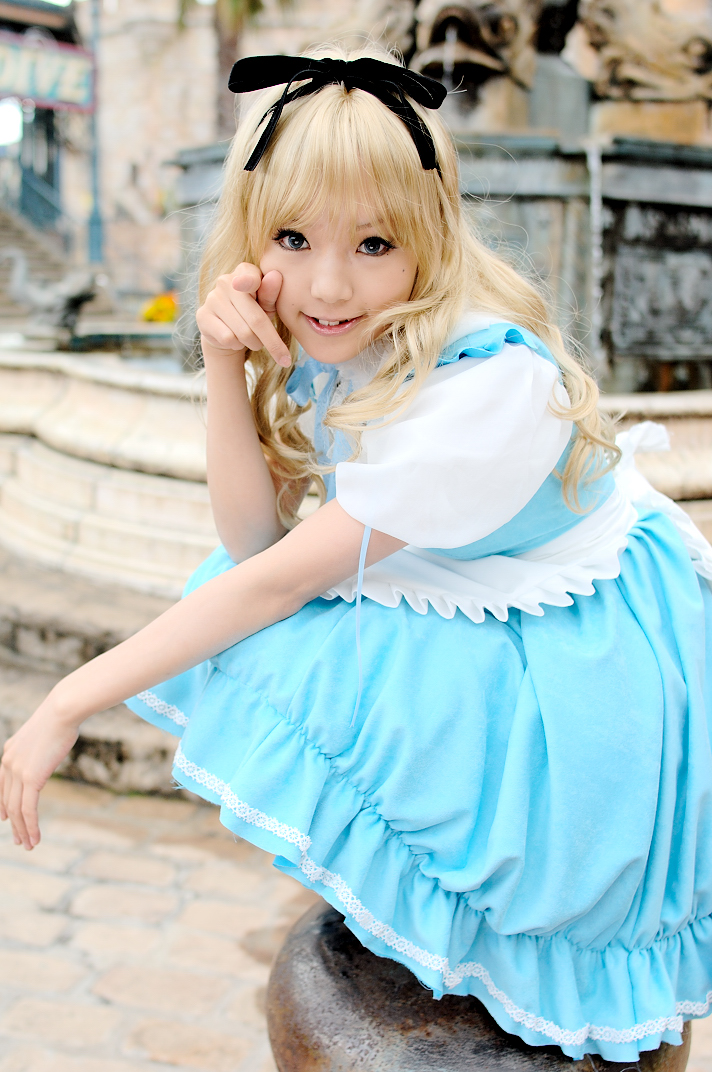 kipi-san, alice (alice in wonderland), alice's adventures in wonderland, photo (medium), 1girl, alice (alice in wonderland) (cosplay), apron, asian, blonde hair, blue eyes, breasts, color contacts, cosplay, female focus, hair ribbon, long hair, looking at viewer, mole, petite, pointing, pointing at viewer, ribbon, small breasts, solo, squatting