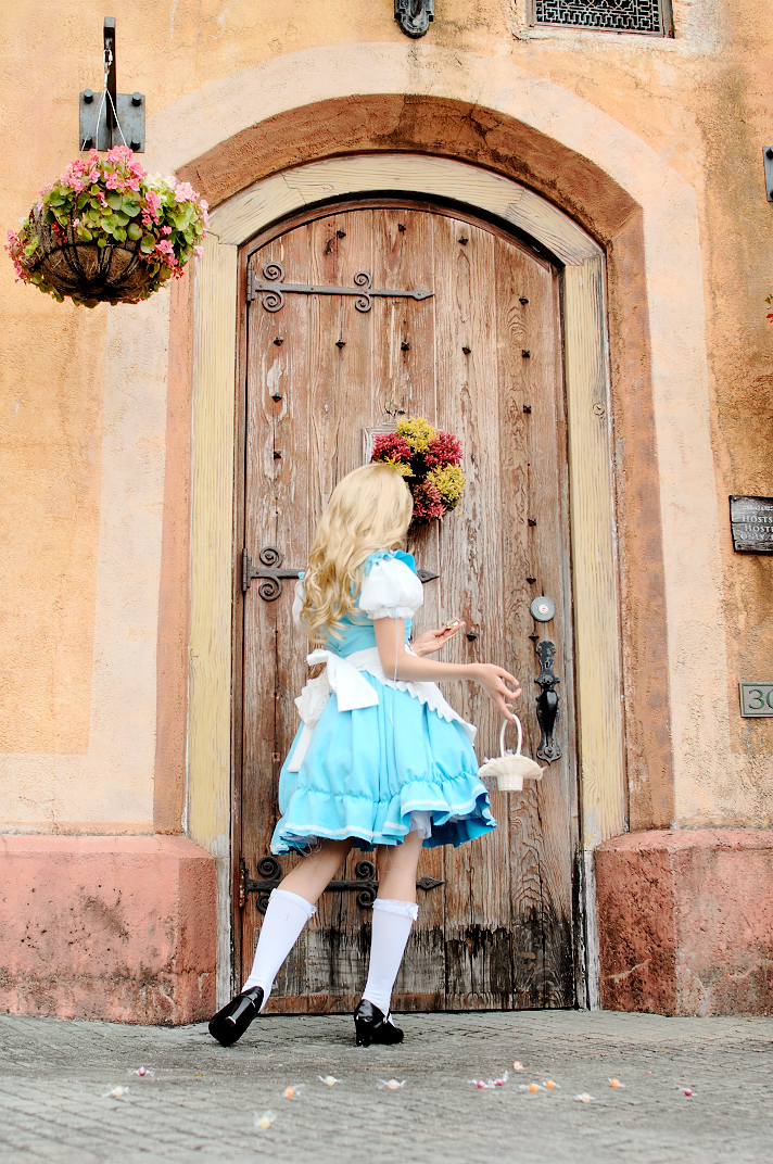 kipi-san, alice (alice in wonderland), alice's adventures in wonderland, photo (medium), 1girl, alice (alice in wonderland) (cosplay), apron, asian, blonde hair, breasts, cosplay, female focus, from behind, hair ribbon, long hair, outdoors, ribbon, small breasts, socks, solo