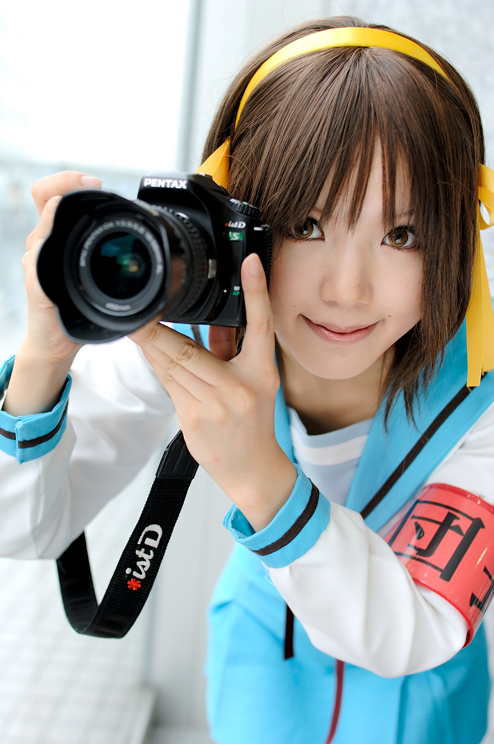 kipi-san, suzumiya haruhi, suzumiya haruhi no yuuutsu, photo (medium), 1girl, armband, asian, brown eyes, brown hair, camera, cosplay, female focus, hair ribbon, hairband, looking at viewer, mole, ribbon, school uniform, serafuku, smile, solo, suzumiya haruhi (cosplay)