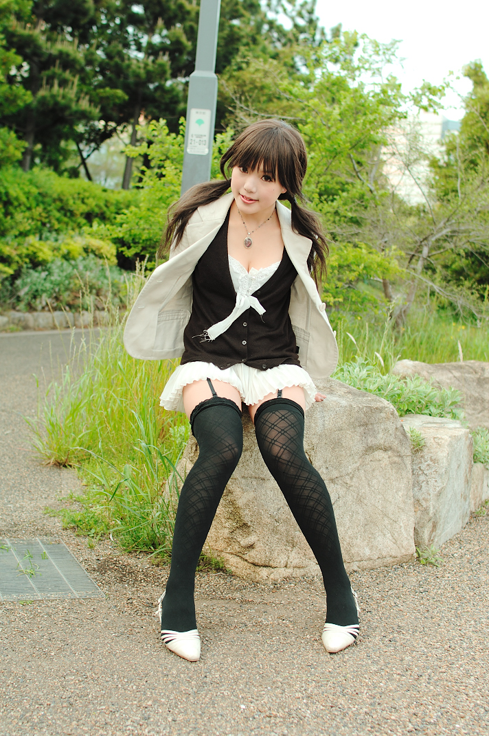 kipi-san, photo (medium), 1girl, asian, black thighhighs, boulder, breasts, cleavage, dutch angle, female focus, garter straps, jewelry, long hair, looking at viewer, miniskirt, mole, necklace, outdoors, pigeon-toed, pleated skirt, rock, shoes, sitting, skirt, small breasts, solo, thighhighs, tree, twintails, zettai ryouiki