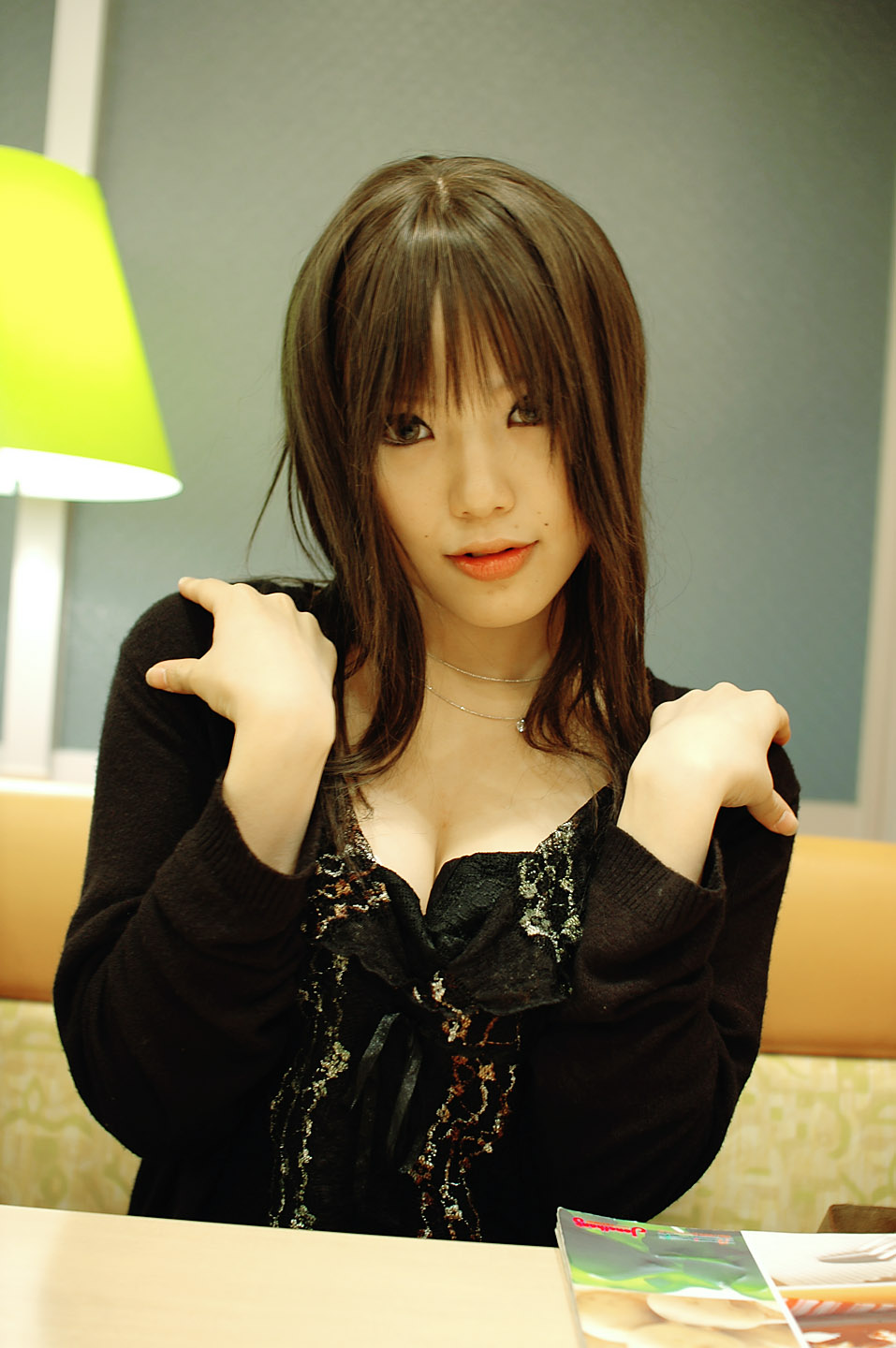 kipi-san, highres, photo (medium), 1girl, asian, breasts, breasts squeezed together, brown eyes, brown hair, cardigan, cleavage, dress, dutch angle, female focus, indoors, jewelry, lipstick, long hair, looking at viewer, makeup, mascara, mole, necklace, sitting, small breasts, solo, table