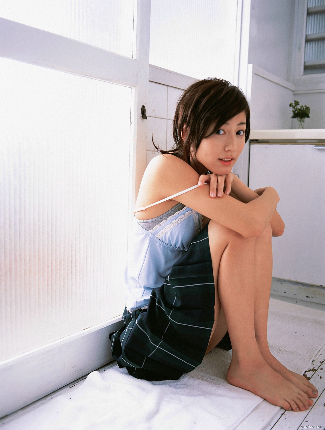 sugimoto yumi, highres, photo (medium), 1girl, asian, barefoot, bra, brown hair, camisole, female focus, hugging own legs, indoors, lingerie, long hair, looking at viewer, miniskirt, on floor, pleated skirt, sitting, skirt, solo, underwear