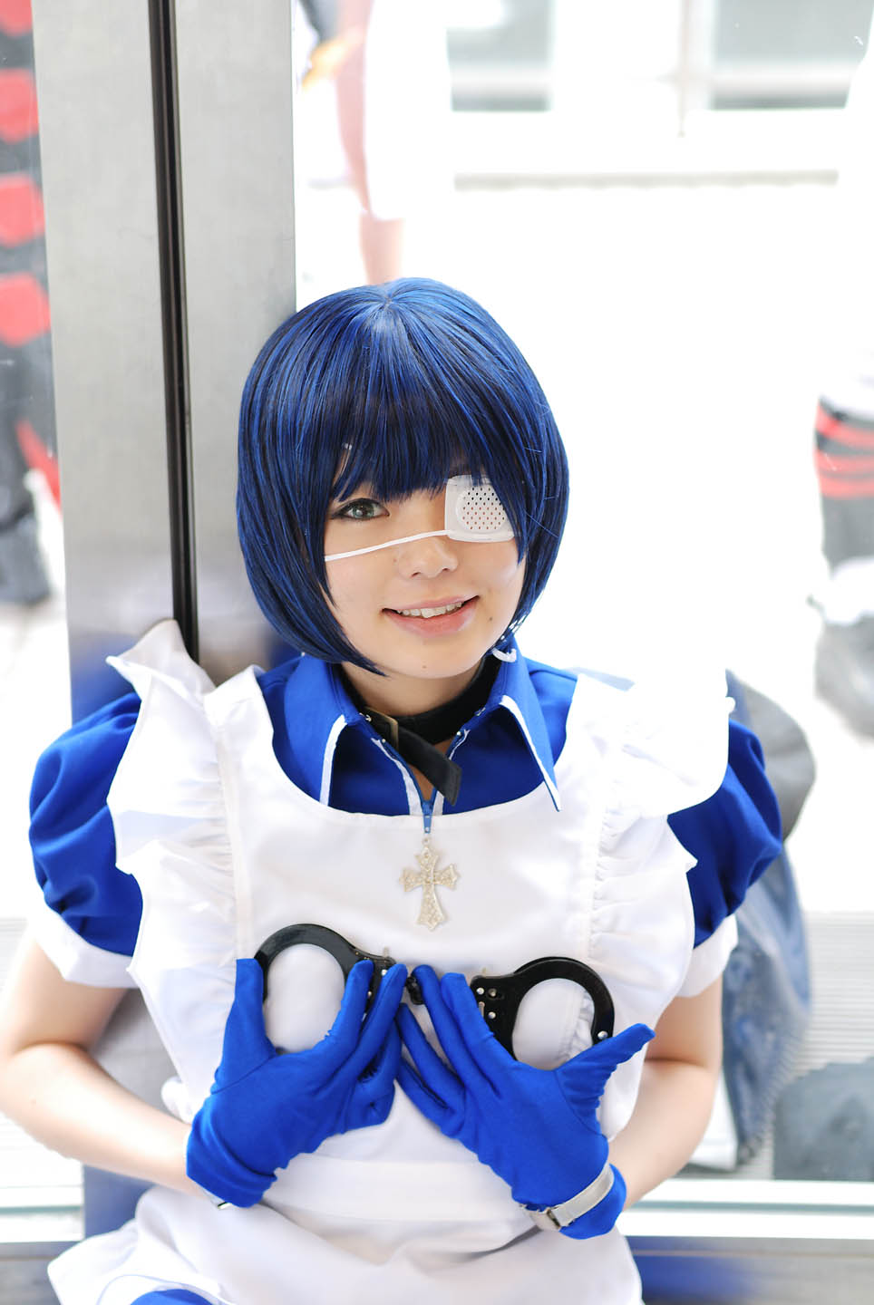 namada, ryomou shimei, ikkitousen, cosplay photo, highres, photo (medium), 1girl, apron, asian, blue eyes, blue gloves, blue hair, blurry, collar, color contacts, contrapposto, cosplay, cross, cuffs, depth of field, eyepatch, female focus, gloves, handcuffs, indoors, looking at viewer, maid, maid apron, mole, puffy short sleeves, puffy sleeves, ryomou shimei (cosplay), short sleeves, smile, solo, standing