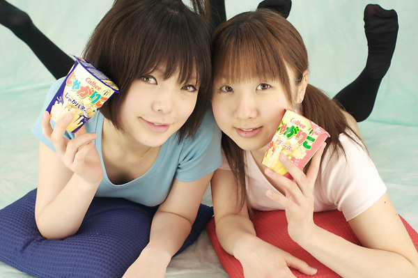 miasa, namada, black legwear, photo (medium), 2girls, asian, black hair, brown eyes, brown hair, color contacts, feet, food, indoors, long hair, looking at viewer, lying, multiple girls, no shoes, on stomach, pillow, shirt, short hair, smile, snack, t-shirt, thighhighs, twintails