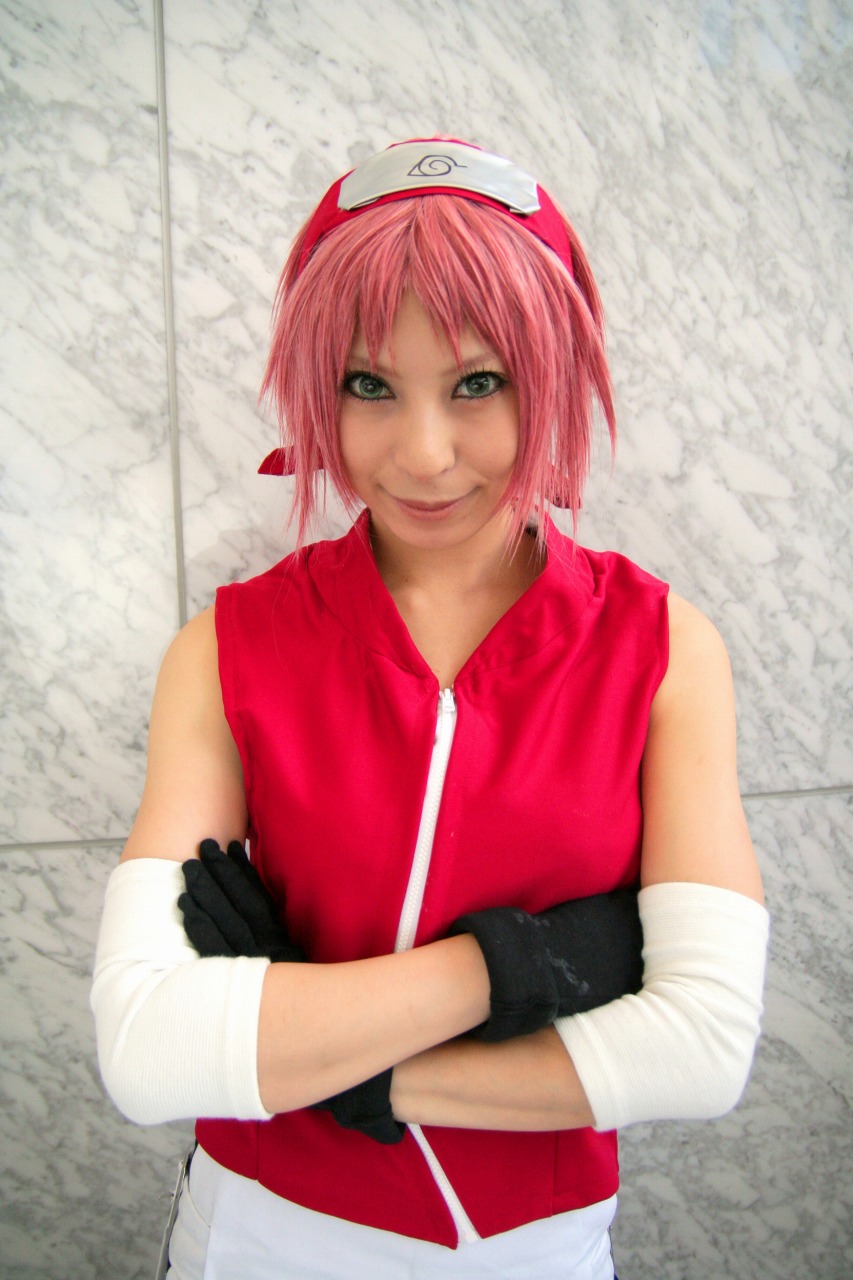 ari, haruno sakura, naruto (series), naruto shippuuden, highres, photo (medium), 1girl, arm warmers, bare shoulders, black gloves, cosplay, crossed arms, eyelashes, female focus, gloves, green eyes, haruno sakura (cosplay), headband, headdress, konohagakure symbol, lips, looking at viewer, miniskirt, pink hair, red shirt, shirt, short hair, shorts, skirt, sleeveless, sleeveless shirt, smile, solo, upper body, white skirt