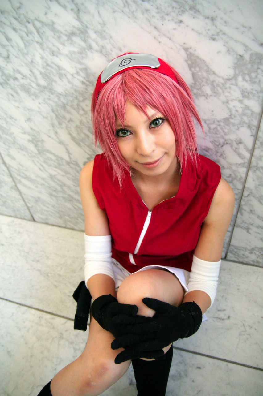 ari, haruno sakura, naruto (series), naruto shippuuden, highres, photo (medium), 1girl, arm warmers, bare shoulders, black gloves, black socks, cosplay, eyelashes, female focus, gloves, green eyes, hand up, haruno sakura (cosplay), head tilt, headband, headdress, holster, konohagakure symbol, lips, looking at viewer, looking up, miniskirt, pink hair, red shirt, shirt, short hair, shorts, shorts under skirt, sitting, skirt, sleeveless, sleeveless shirt, smile, socks, solo, thigh holster, white skirt