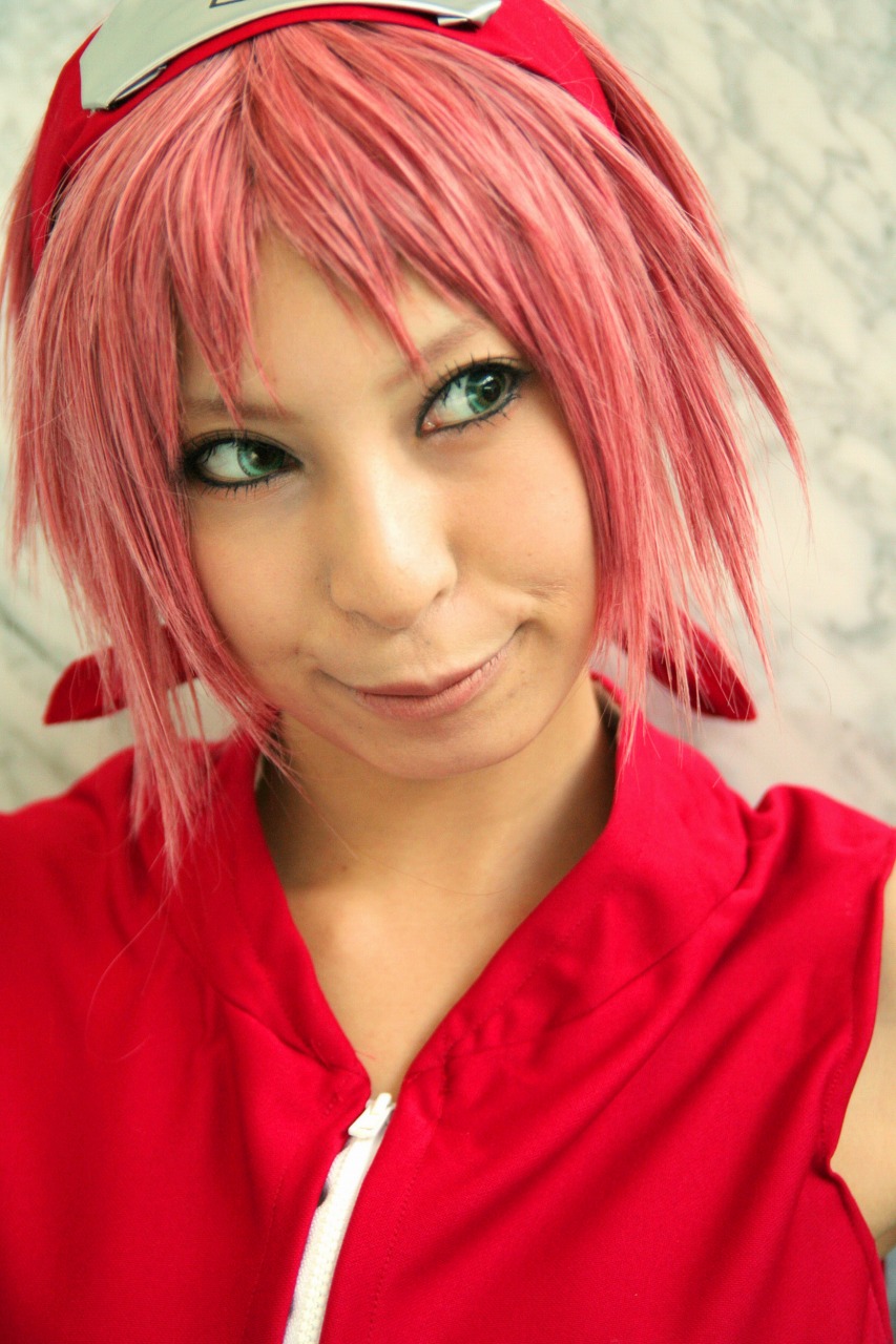 ari, haruno sakura, naruto (series), naruto shippuuden, highres, photo (medium), 1girl, bare shoulders, cosplay, female focus, gloves, green eyes, haruno sakura (cosplay), headband, headdress, konohagakure symbol, lips, looking to the side, pink hair, red shirt, shirt, short hair, sleeveless, sleeveless shirt, smile, solo, upper body, zipper