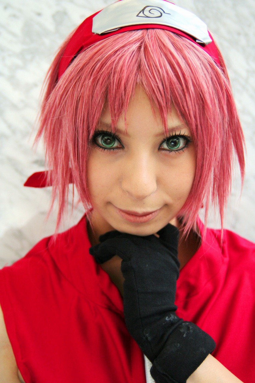 ari, haruno sakura, naruto (series), naruto shippuuden, highres, photo (medium), 1girl, bare shoulders, black gloves, cosplay, female focus, gloves, green eyes, haruno sakura (cosplay), headband, headdress, konohagakure symbol, lips, looking at viewer, pink hair, red shirt, shirt, short hair, sleeveless, sleeveless shirt, smile, solo, upper body