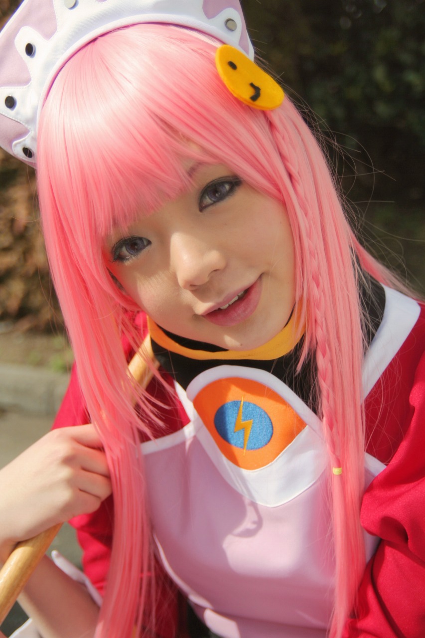 namada, nono (top wo nerae 2!), top wo nerae! (series), top wo nerae 2!, highres, photo (medium), 1girl, apron, asian, blurry, braid, breasts, broom, color contacts, cosplay, depth of field, dress, female focus, head tilt, hedge, japanese (nationality), looking at viewer, maid, maid apron, makeup, mascara, outdoors, parking lot, parted lips, pink hair, puffy sleeves, side braid, sidelocks, small breasts, smile, solo, standing, tree