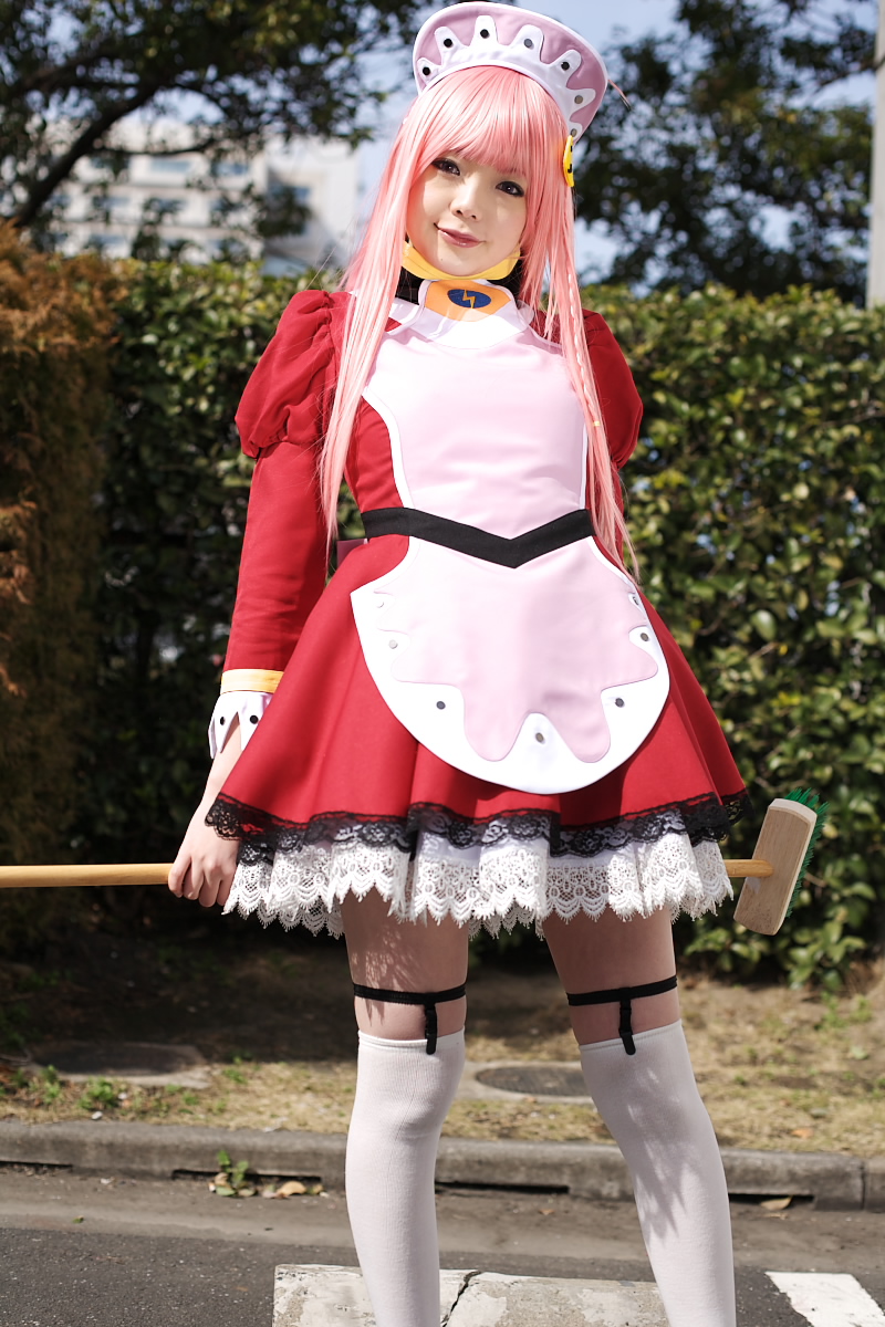 namada, nono (top wo nerae 2!), top wo nerae! (series), top wo nerae 2!, highres, photo (medium), 1girl, apron, asian, blurry, breasts, broom, cosplay, cowboy shot, depth of field, dress, female focus, garter straps, hedge, light smile, looking at viewer, maid, maid apron, makeup, mascara, outdoors, parking lot, pink hair, puffy sleeves, short dress, sidelocks, small breasts, solo, standing, thighhighs, tree, white thighhighs, zettai ryouiki