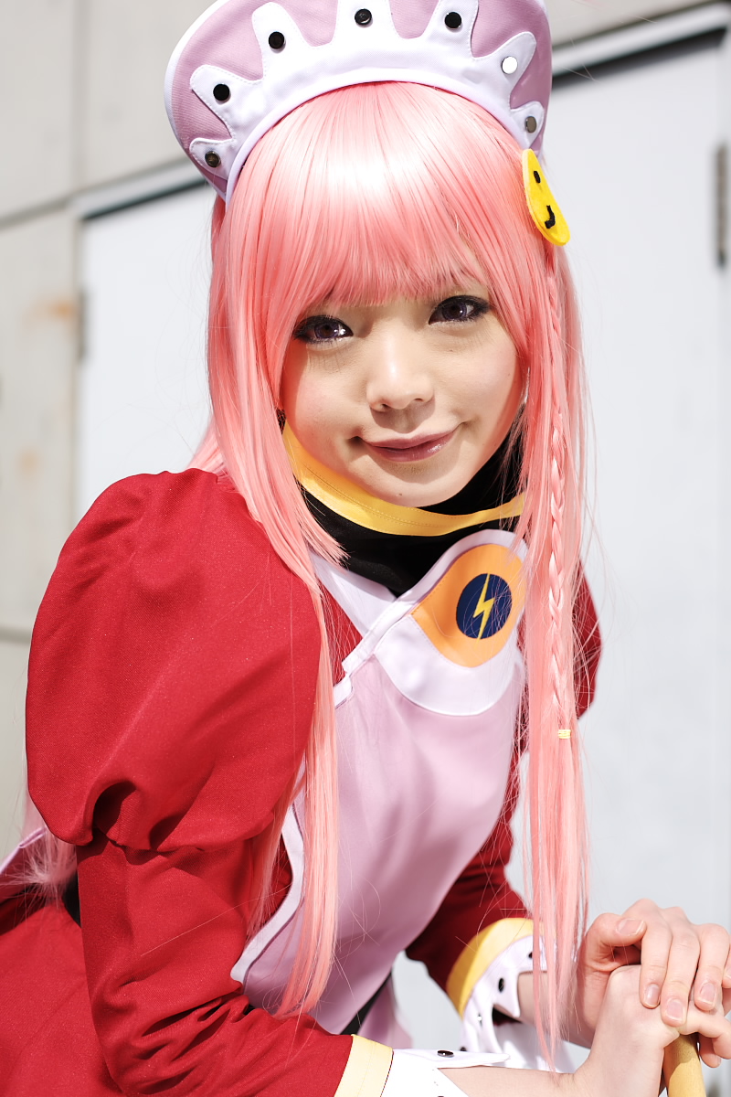 namada, nono (top wo nerae 2!), top wo nerae! (series), top wo nerae 2!, highres, photo (medium), 1girl, apron, asian, blurry, braid, breasts, broom, cosplay, cowboy shot, depth of field, dress, female focus, light smile, looking at viewer, maid, maid apron, makeup, mascara, outdoors, pink hair, puffy sleeves, side braid, sidelocks, small breasts, solo