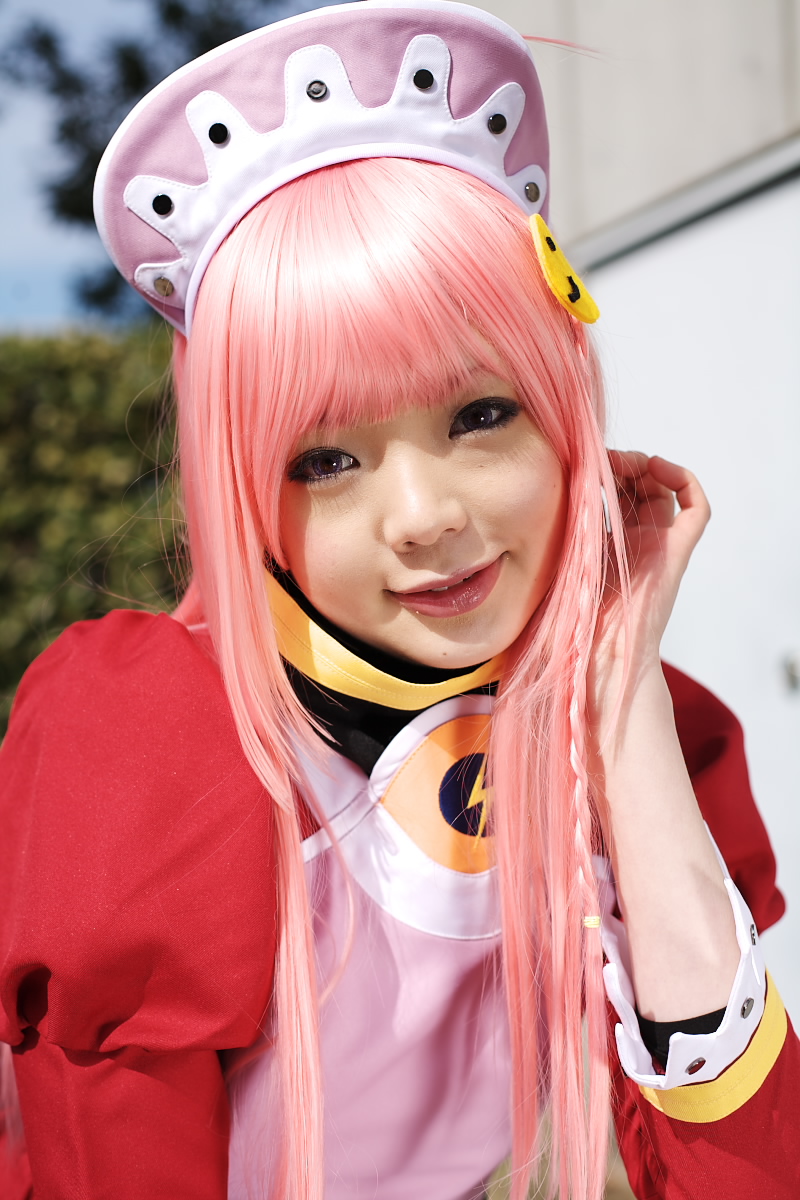 namada, nono (top wo nerae 2!), top wo nerae! (series), top wo nerae 2!, highres, photo (medium), 1girl, apron, asian, blurry, braid, breasts, color contacts, cosplay, depth of field, dress, female focus, head tilt, hedge, light smile, looking at viewer, maid, maid apron, makeup, mascara, mole, outdoors, pink hair, puffy sleeves, side braid, sidelocks, small breasts, solo