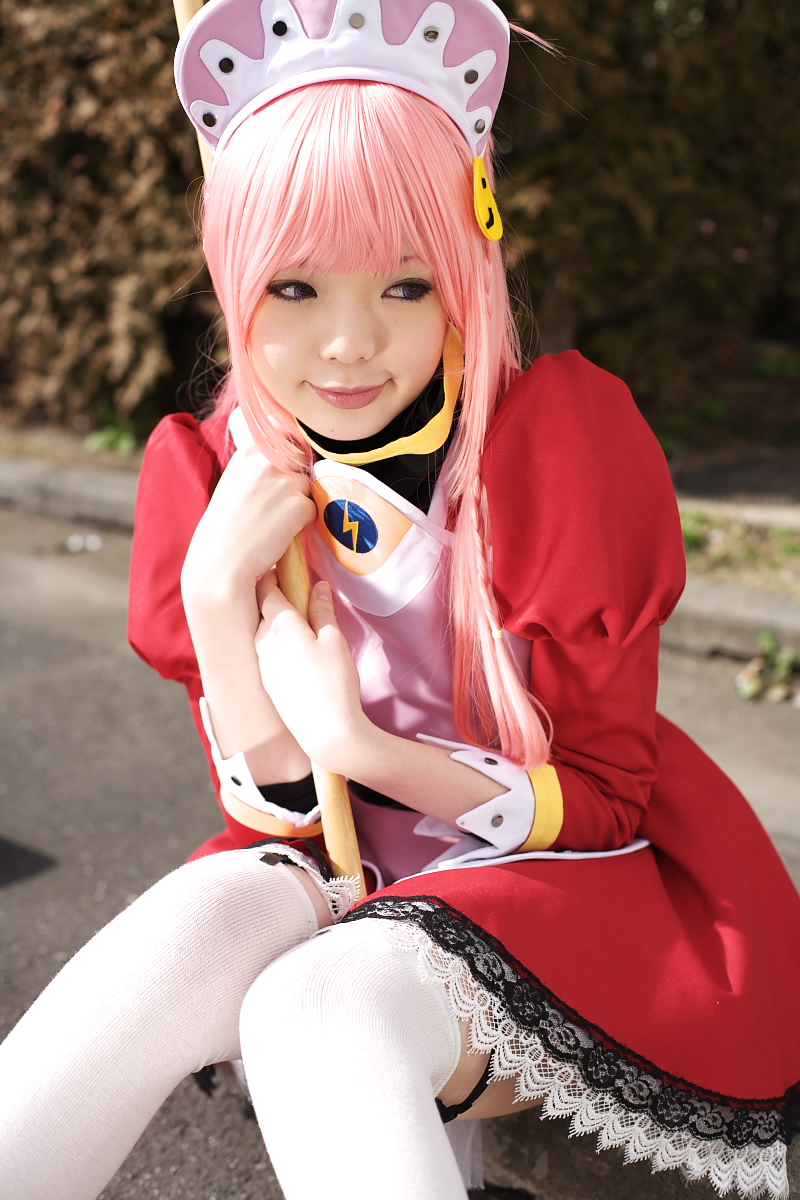 namada, nono (top wo nerae 2!), top wo nerae! (series), top wo nerae 2!, highres, photo (medium), 1girl, apron, asian, between legs, blurry, breasts, broom, cosplay, depth of field, dress, female focus, head tilt, hedge, knees together feet apart, looking to the side, maid, maid apron, makeup, mascara, outdoors, parking lot, pink hair, puffy sleeves, sidelocks, sitting, small breasts, solo, thighhighs, white thighhighs