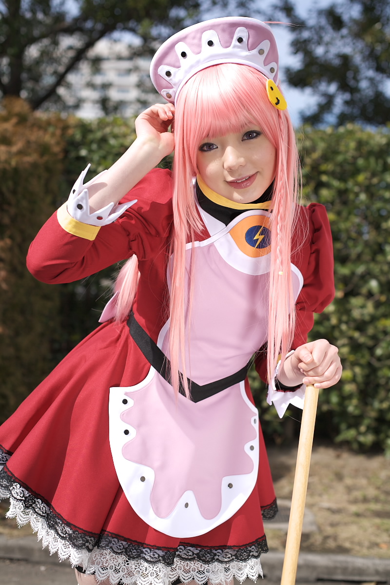namada, nono (top wo nerae 2!), top wo nerae! (series), top wo nerae 2!, highres, photo (medium), 1girl, apron, asian, blurry, breasts, broom, cosplay, cowboy shot, depth of field, dress, female focus, garter straps, hedge, light smile, looking at viewer, maid, maid apron, makeup, mascara, outdoors, parking lot, pink hair, puffy sleeves, short dress, sidelocks, small breasts, solo, standing, thighhighs, tree, white thighhighs, zettai ryouiki