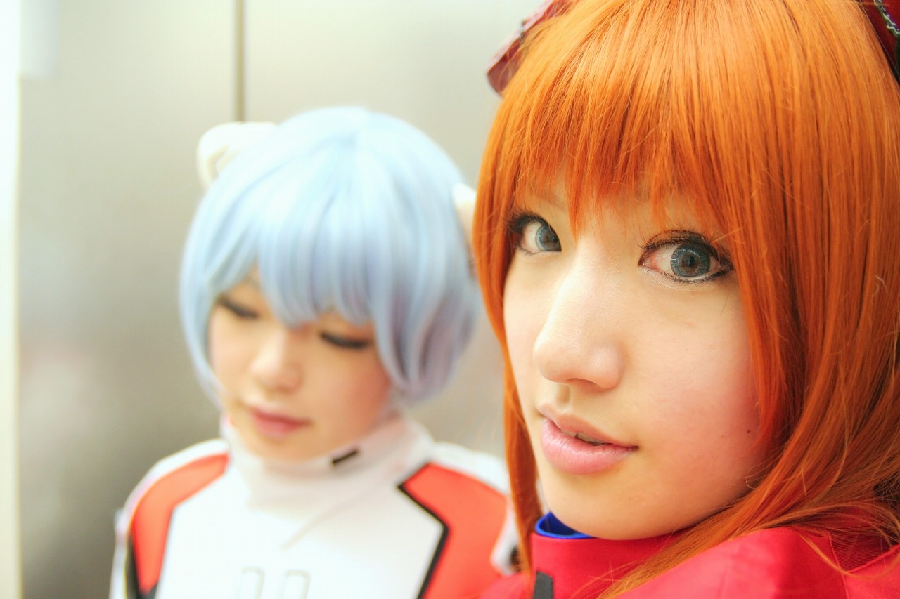 namada, saya (cosplayer), ayanami rei, souryuu asuka langley, neon genesis evangelion, photo (medium), 2girls, asian, ayanami rei (cosplay), blue eyes, blue hair, blurry, blurry background, color contacts, cosplay, depth of field, hairpods, indoors, long hair, looking at viewer, looking back, makeup, mascara, mecha pilot suit, multiple girls, orange hair, parted lips, plugsuit (cosplay), plugsuit (evangelion), short hair, solo focus, souryuu asuka langley (cosplay), standing