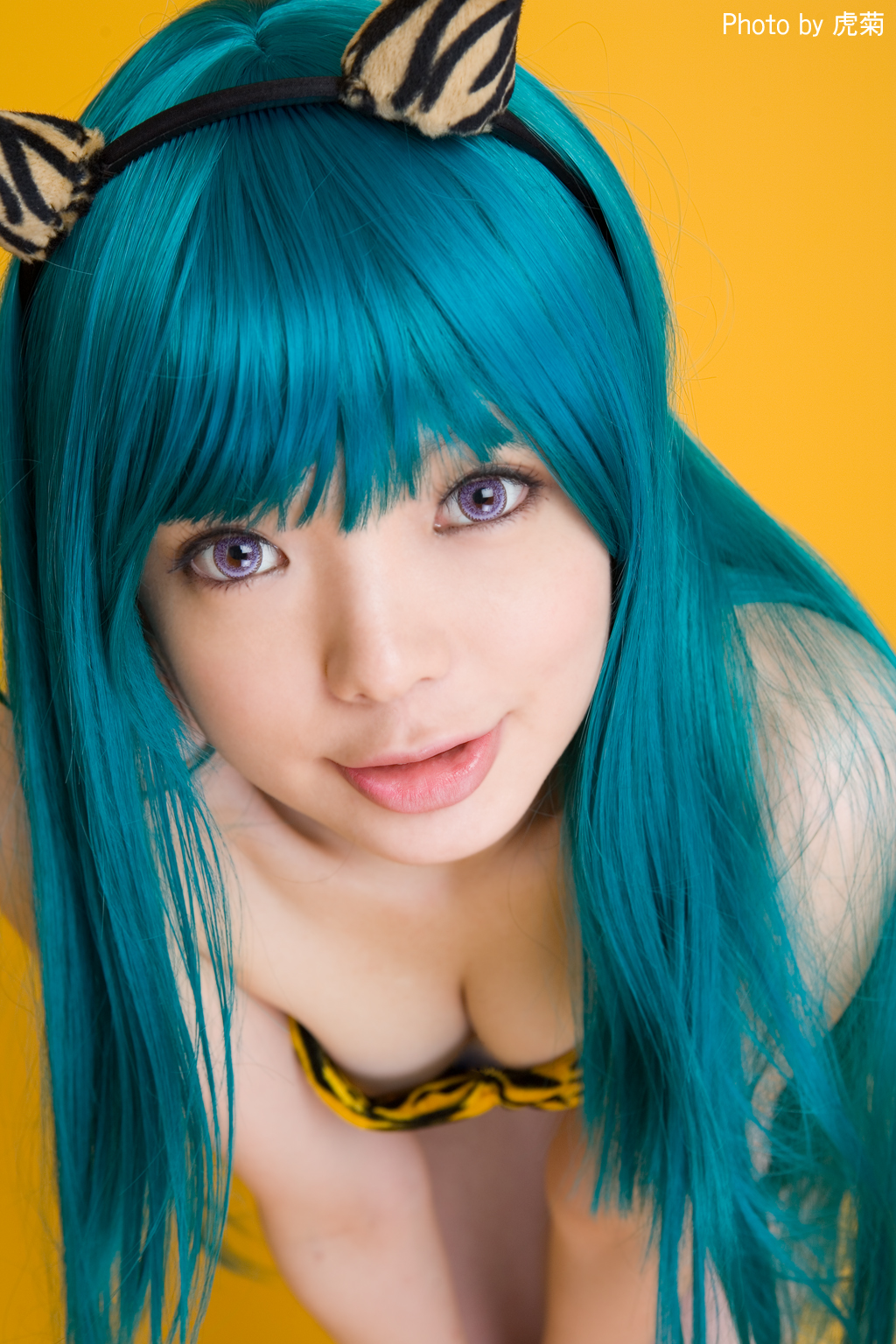 namada, lum, urusei yatsura, highres, photo (medium), 1girl, animal print, aqua hair, asian, bikini, blue hair, blurry, breasts, cleavage, color contacts, cosplay, depth of field, fake horns, female focus, horns, indoors, leaning forward, light smile, long hair, looking at viewer, lum (cosplay), purple eyes, simple background, small breasts, solo, strapless, strapless bikini, swimsuit, tiger print, yellow background