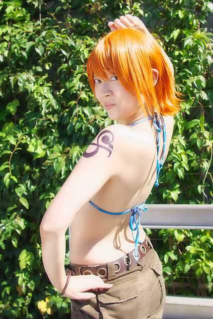 amanone shun, nami (one piece), nami (one piece) (skypiea), one piece, photo (medium), 1girl, asian, belt, bikini, bikini top only, bracelet, brown eyes, camouflage, cargo shorts, cosplay, female focus, jewelry, looking at viewer, midriff, nami (one piece) (cosplay), orange hair, outdoors, plant, shorts, shoulder tattoo, skypiea, solo, swimsuit, tattoo