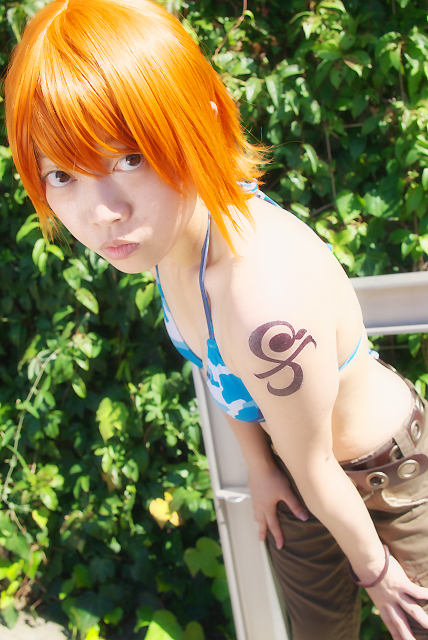 amanone shun, nami (one piece), nami (one piece) (skypiea), one piece, photo (medium), 1girl, asian, belt, bikini, bikini top only, bracelet, brown eyes, camouflage, cargo shorts, cosplay, female focus, jewelry, looking at viewer, midriff, nami (one piece) (cosplay), orange hair, outdoors, plant, shorts, shoulder tattoo, skypiea, solo, swimsuit, tattoo