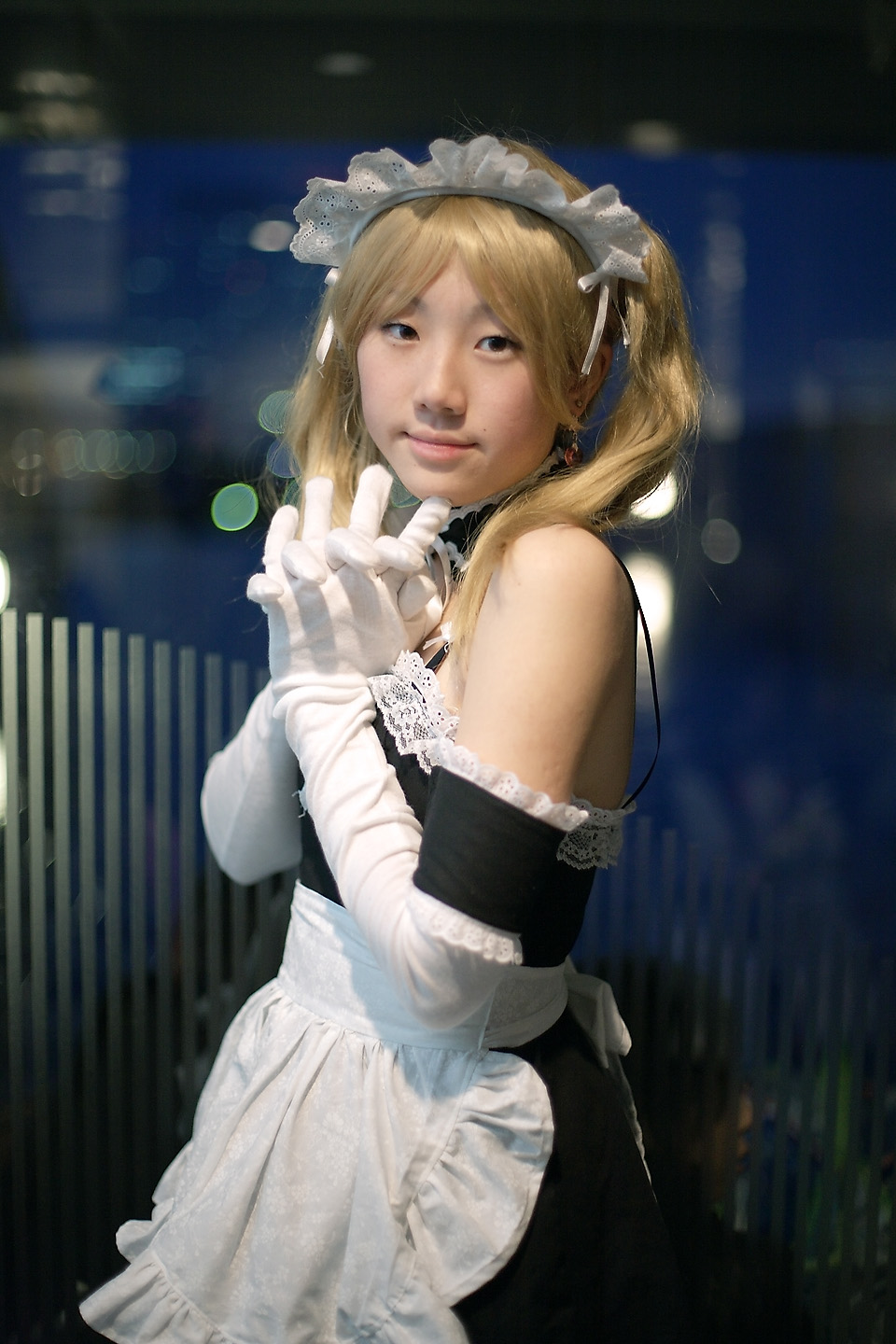 hime (cosplayer), sawatari izumi, kore ga watashi no goshujin-sama, highres, photo (medium), 1girl, apron, asian, bare shoulders, blonde hair, blurry, cosplay, cowboy shot, depth of field, detached collar, earrings, elbow gloves, female focus, gloves, indoors, japanese (nationality), jewelry, looking at viewer, maid, maid apron, maid headdress, nakabayashi yoshitaka's maid uniform, night, sawatari izumi (cosplay), solo, twintails, white gloves
