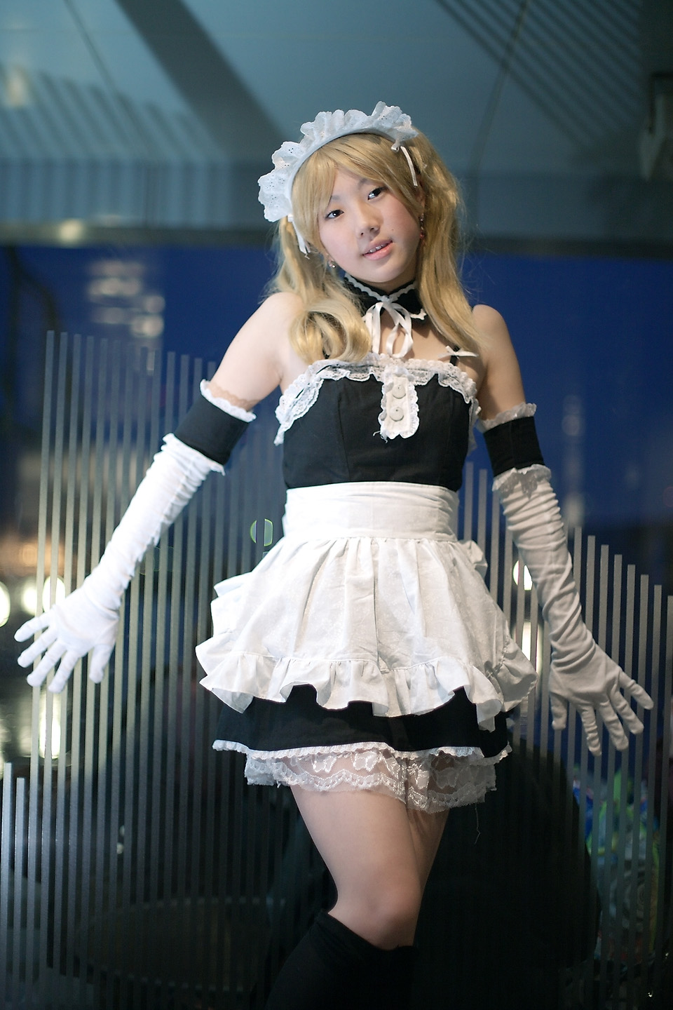 hime (cosplayer), sawatari izumi, kore ga watashi no goshujin-sama, highres, photo (medium), 1girl, apron, asian, bare shoulders, blonde hair, blurry, cosplay, depth of field, detached collar, earrings, elbow gloves, feet out of frame, female focus, gloves, head tilt, indoors, japanese (nationality), jewelry, kneehighs, looking at viewer, maid, maid apron, maid headdress, nakabayashi yoshitaka's maid uniform, night, sawatari izumi (cosplay), socks, solo, twintails, white gloves