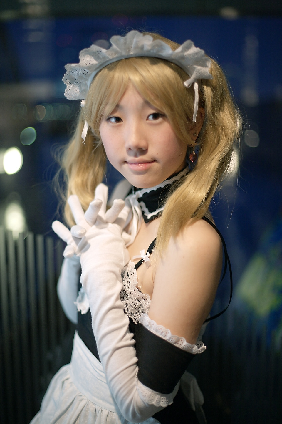 hime (cosplayer), kore ga watashi no goshujin-sama, highres, photo (medium), 1girl, apron, asian, bare shoulders, blonde hair, blurry, cosplay, depth of field, detached collar, earrings, elbow gloves, female focus, gloves, indoors, japanese (nationality), jewelry, looking at viewer, maid, maid apron, maid headdress, nakabayashi yoshitaka's maid uniform, night, sawatari izumi (cosplay), solo, twintails, upper body, white gloves