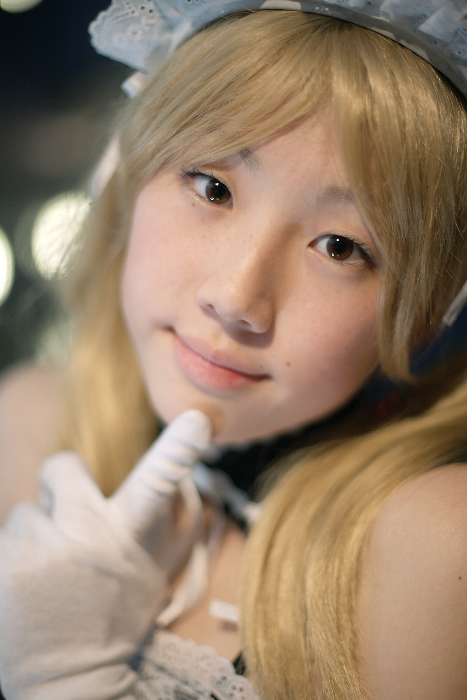 hime (cosplayer), sawatari izumi, kore ga watashi no goshujin-sama, highres, photo (medium), 1girl, apron, asian, bare shoulders, blonde hair, blurry, cosplay, depth of field, detached collar, earrings, elbow gloves, female focus, gloves, indoors, japanese (nationality), jewelry, looking at viewer, maid, maid apron, maid headdress, nakabayashi yoshitaka's maid uniform, sawatari izumi (cosplay), solo, twintails, white gloves