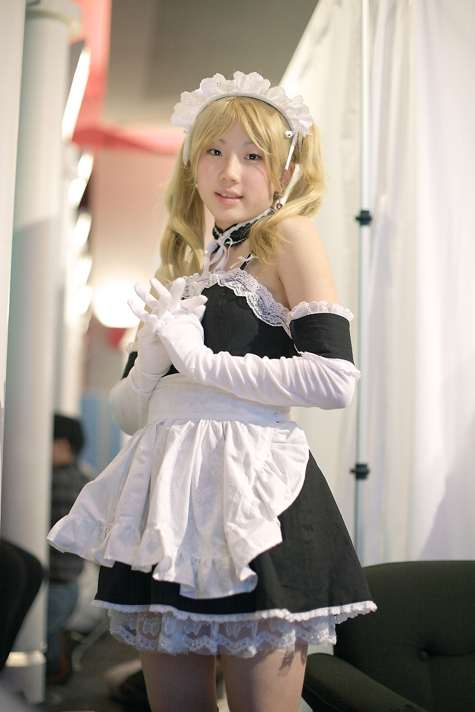 hime (cosplayer), sawatari izumi, kore ga watashi no goshujin-sama, highres, photo (medium), 1girl, apron, asian, bare shoulders, blonde hair, blurry, cosplay, cowboy shot, depth of field, detached collar, earrings, elbow gloves, female focus, gloves, indoors, japanese (nationality), jewelry, looking at viewer, maid, maid apron, maid headdress, nakabayashi yoshitaka's maid uniform, sawatari izumi (cosplay), solo, twintails, white gloves