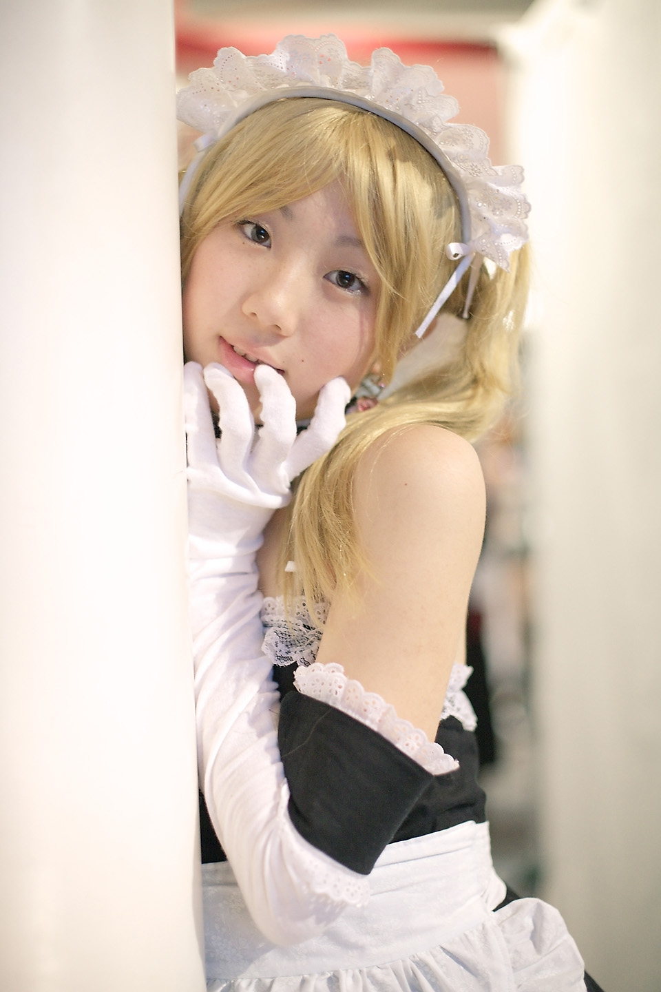 hime (cosplayer), sawatari izumi, kore ga watashi no goshujin-sama, highres, photo (medium), 1girl, apron, asian, bare shoulders, blonde hair, blurry, cosplay, depth of field, detached collar, earrings, elbow gloves, female focus, gloves, indoors, japanese (nationality), jewelry, looking at viewer, maid, maid apron, maid headdress, nakabayashi yoshitaka's maid uniform, sawatari izumi (cosplay), solo, twintails, white gloves