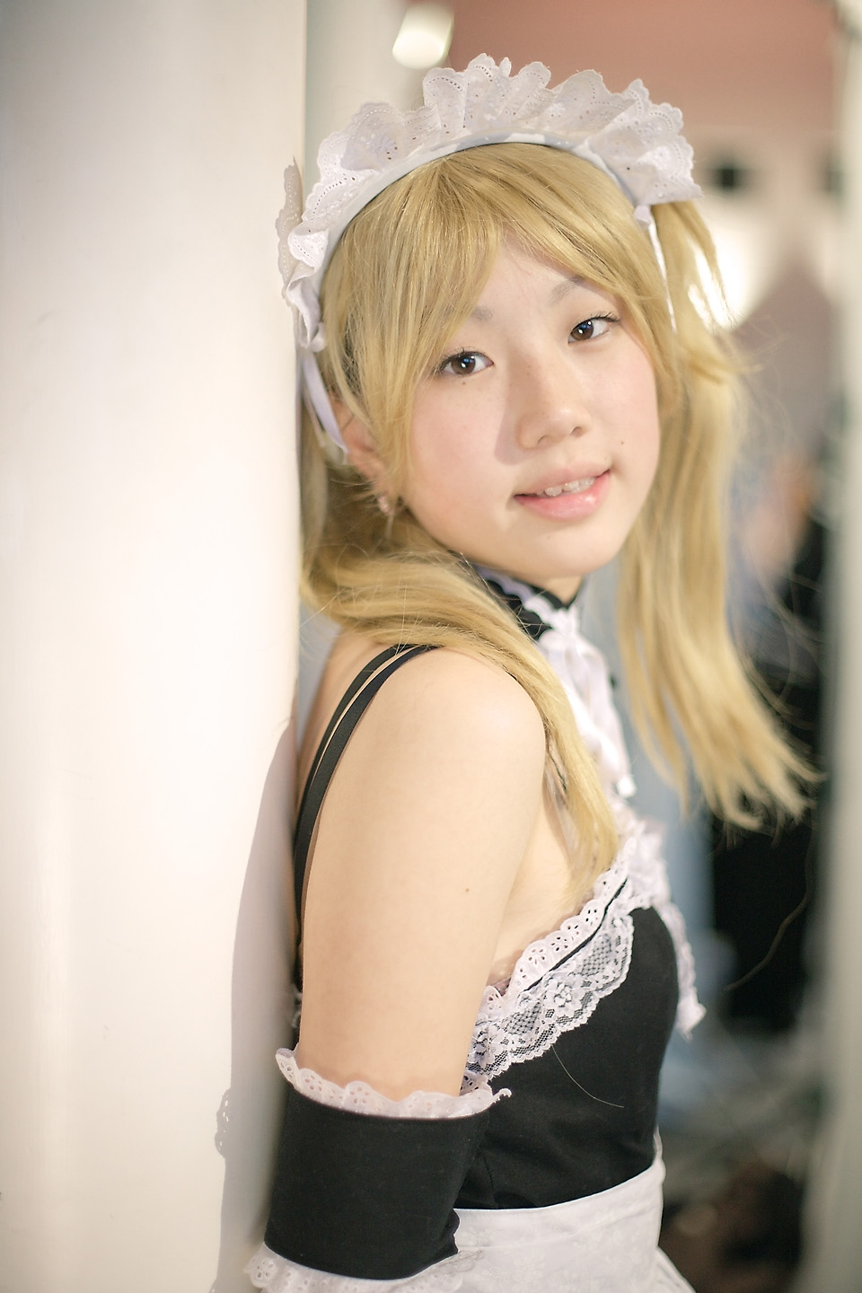 hime (cosplayer), sawatari izumi, kore ga watashi no goshujin-sama, highres, photo (medium), 1girl, apron, asian, bare shoulders, blonde hair, blurry, cosplay, depth of field, detached collar, earrings, elbow gloves, female focus, gloves, indoors, japanese (nationality), jewelry, looking at viewer, maid, maid apron, maid headdress, nakabayashi yoshitaka's maid uniform, sawatari izumi (cosplay), solo, twintails, upper body, white gloves