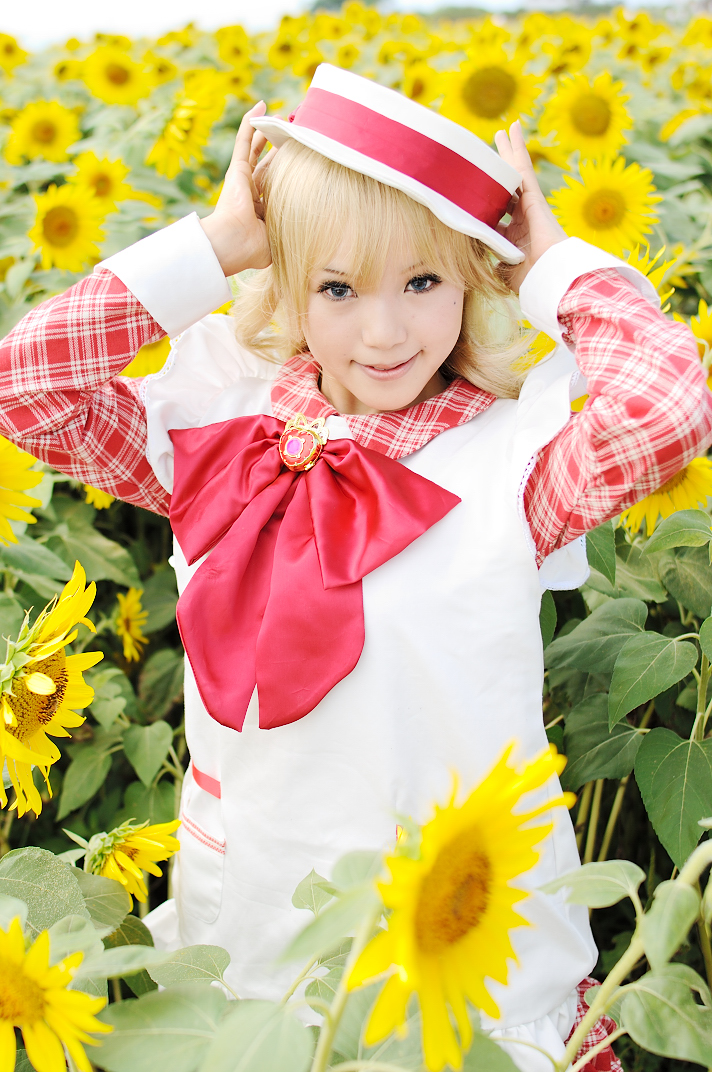 kipi-san, nadja applefield, ashita no nadja, photo (medium), 1girl, apron, asian, blonde hair, blurry, boater hat, bow, cosplay, depth of field, female focus, flower, frills, hat, long hair, looking at viewer, mole, nadja applefield (cosplay), outdoors, solo, standing, sunflower