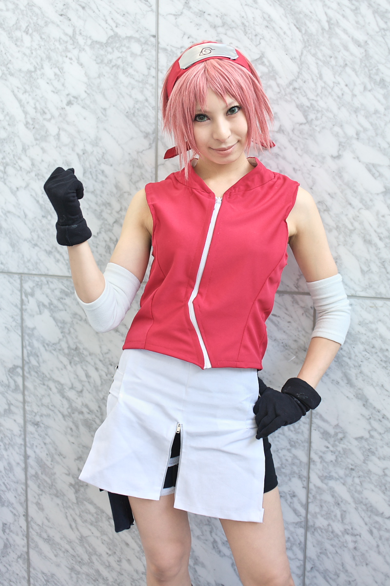 ari, haruno sakura, naruto (series), naruto shippuuden, highres, photo (medium), 1girl, arm warmers, bare shoulders, black gloves, cosplay, eyelashes, female focus, gloves, green eyes, hand up, haruno sakura (cosplay), head tilt, headband, headdress, holster, konohagakure symbol, lips, looking at viewer, miniskirt, pink hair, red shirt, shirt, short hair, shorts, shorts under skirt, side slit, skirt, sleeveless, sleeveless shirt, smile, solo, thigh holster, thigh strap, white skirt