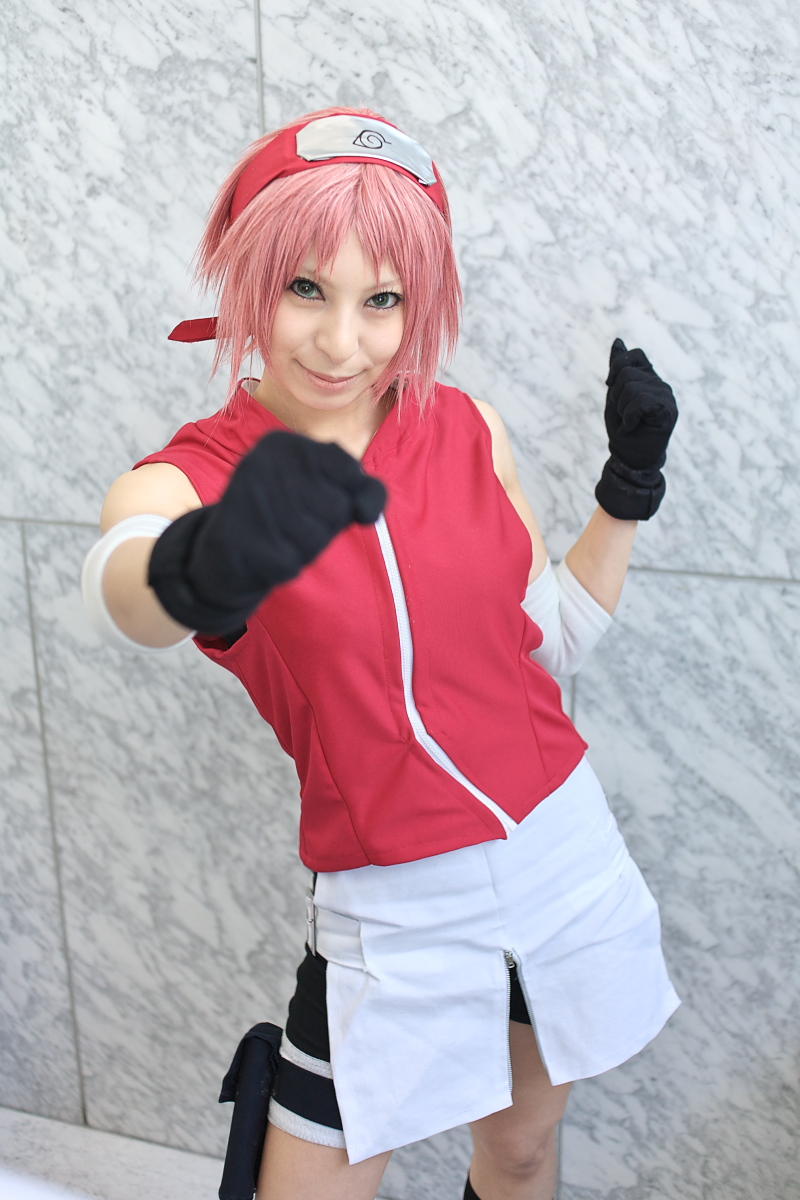 ari, haruno sakura, naruto (series), naruto shippuuden, highres, photo (medium), 1girl, arm warmers, bare shoulders, black gloves, blurry, cosplay, depth of field, eyelashes, female focus, foreshortening, gloves, green eyes, hand up, haruno sakura (cosplay), head tilt, headband, headdress, holster, konohagakure symbol, lips, looking at viewer, miniskirt, pink hair, red shirt, shirt, short hair, shorts, shorts under skirt, side slit, skirt, sleeveless, sleeveless shirt, smile, solo, thigh holster, thigh strap, white skirt