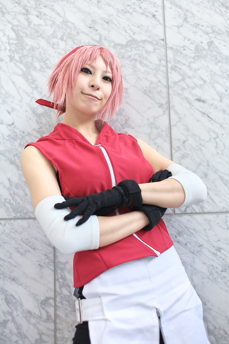 ari, haruno sakura, naruto (series), naruto shippuuden, highres, photo (medium), 1girl, arm warmers, bare shoulders, black gloves, cosplay, crossed arms, eyelashes, female focus, gloves, green eyes, haruno sakura (cosplay), head tilt, headband, headdress, konohagakure symbol, lips, looking at viewer, miniskirt, pink hair, red shirt, shirt, short hair, shorts, side slit, skirt, sleeveless, sleeveless shirt, smile, solo, upper body, white skirt