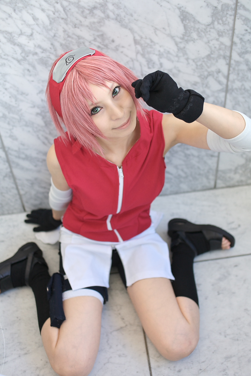ari, haruno sakura, naruto (series), naruto shippuuden, highres, photo (medium), 1girl, arm warmers, bandages, bare shoulders, bike shorts, black gloves, black shoes, black socks, blurry, cosplay, depth of field, eyelashes, female focus, gloves, green eyes, hand up, haruno sakura (cosplay), head tilt, headband, headdress, holster, konohagakure symbol, lips, looking at viewer, looking up, miniskirt, pink hair, red shirt, shirt, shoes, short hair, shorts, shorts under skirt, side slit, sitting, skirt, sleeveless, sleeveless shirt, smile, socks, solo, thigh holster, thigh strap, toeless legwear, toes, wariza, white skirt